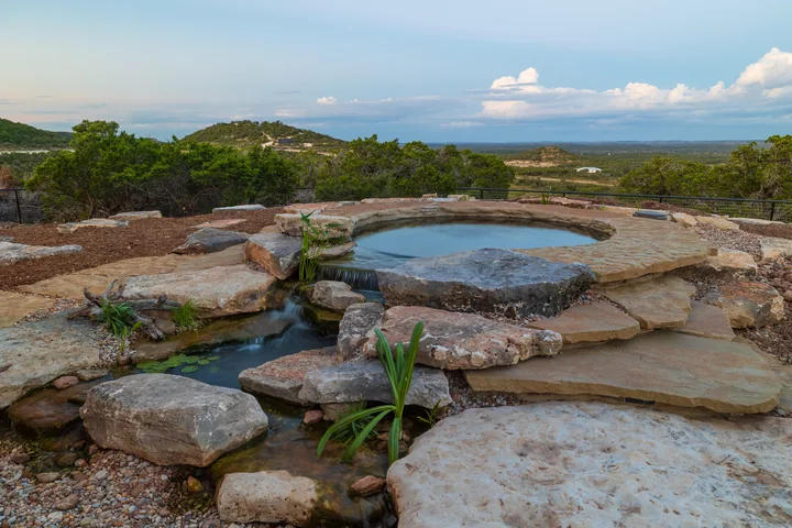 A hilltop stone pool in daylight beneath a broad sky and Hill Country horizon