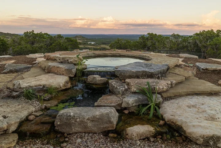 A hilltop stone pool with a negative edge overlooking the Hill Country at sunset