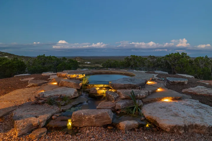 A lit stone pool on a hilltop at dusk overlooking the Texas Hill Country
