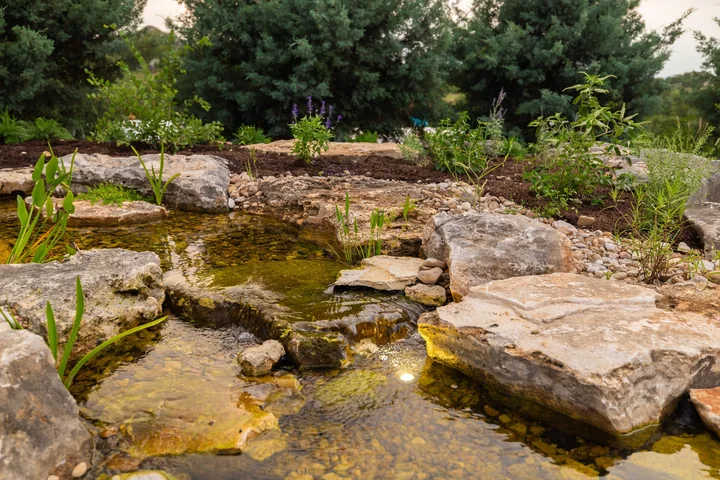 A shallow limestone stream running through planting beside a limestone house